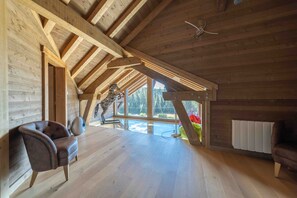 A spacious room with wooden beams, a large window, and a ceiling fan. - Chalet 'L'Alpage' with Mountain View, Sauna and Jacuzzi (Gérardmer)