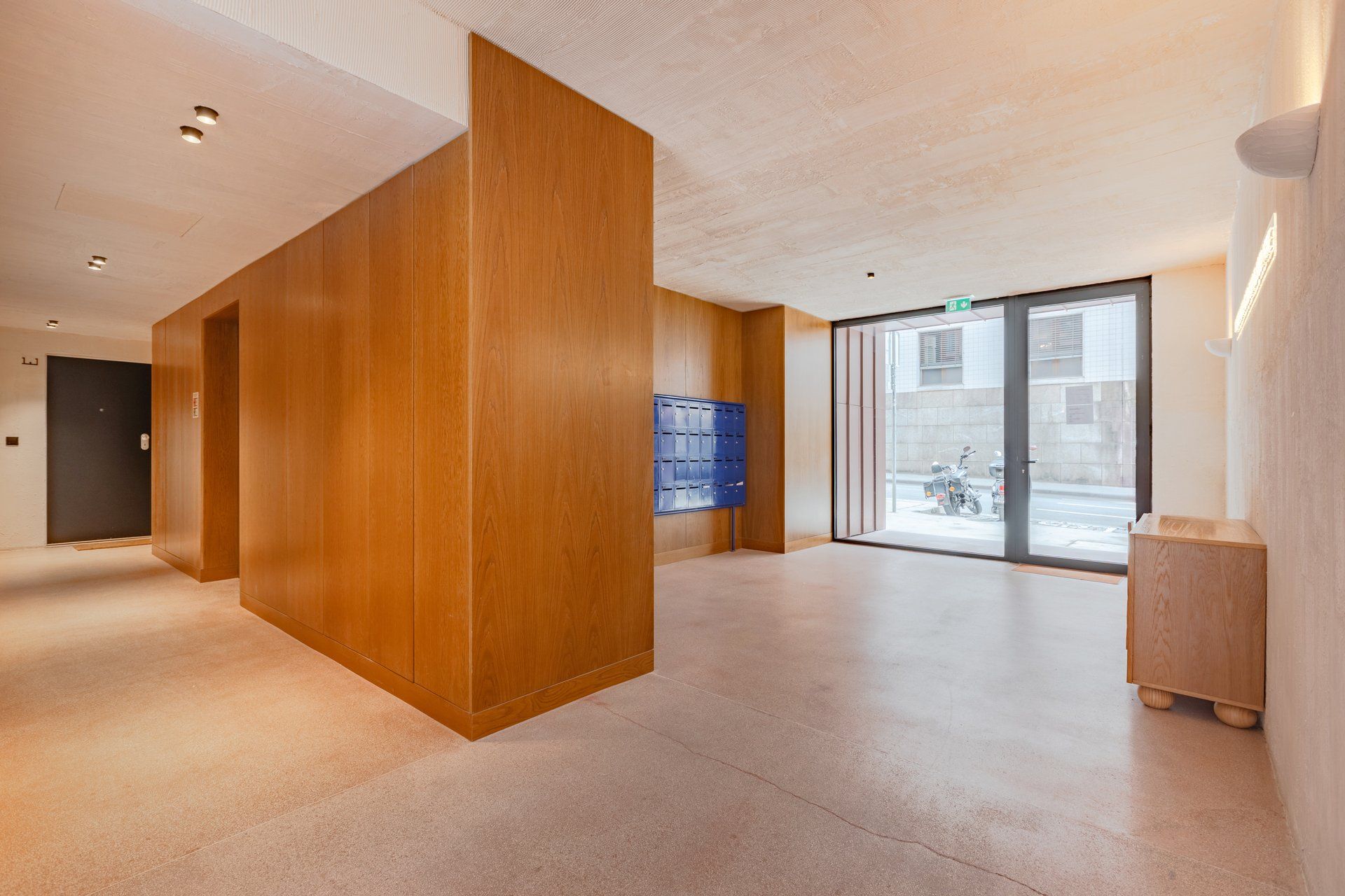 Een modern interieur met een houten accentmuur, een blauwe opbergunit en uitzicht door een glazen deur.