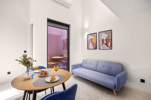 Ein modernes Wohnzimmer mit einem blauen Sofa, einem Holzespeisetisch mit Frühstücksgebäck und abstrakter Kunst an der Wand.