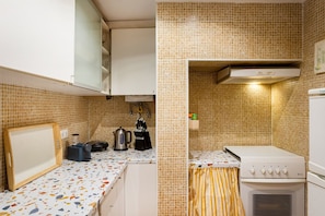 A compact kitchen with a tiled backsplash, a stove, a sink, and a countertop with a kettle and utensils. - Alfama 2BR near Sé & Terreiro do Paço (Lisbon)