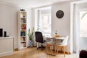 Una sala de estar moderna con una estantería, una mesa de comedor con sillas, una planta en maceta y un reloj de pared.