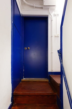 A blue door with a brass doorknob, leading to a wooden staircase with a white wall on one side and a blue wall on the other. - Alfama 2BR near Sé & Terreiro do Paço (Lisbon)
