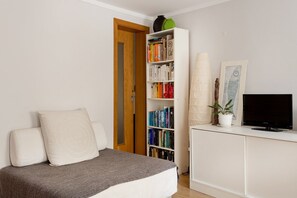 A room with a bed, a bookshelf, a television, and a door leading to another room. - Alfama 2BR near Sé & Terreiro do Paço (Lisbon)