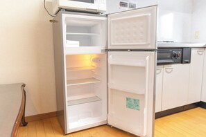 A white refrigerator with a microwave above it, in a kitchen with wooden flooring and white cabinets.