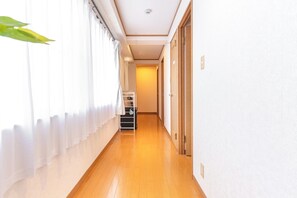 A narrow hallway with a wooden floor, white walls, and a door at the end.