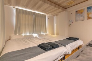 A hotel room with a large bed, two bedside tables, a window with curtains, and a painting on the wall.