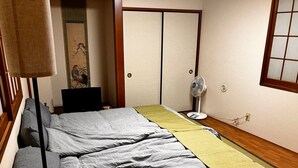 A bedroom with a bed, a bedside table, a fan, and a sliding door. - GrandHOUSE SHINJUKU 301 (Nakano City)