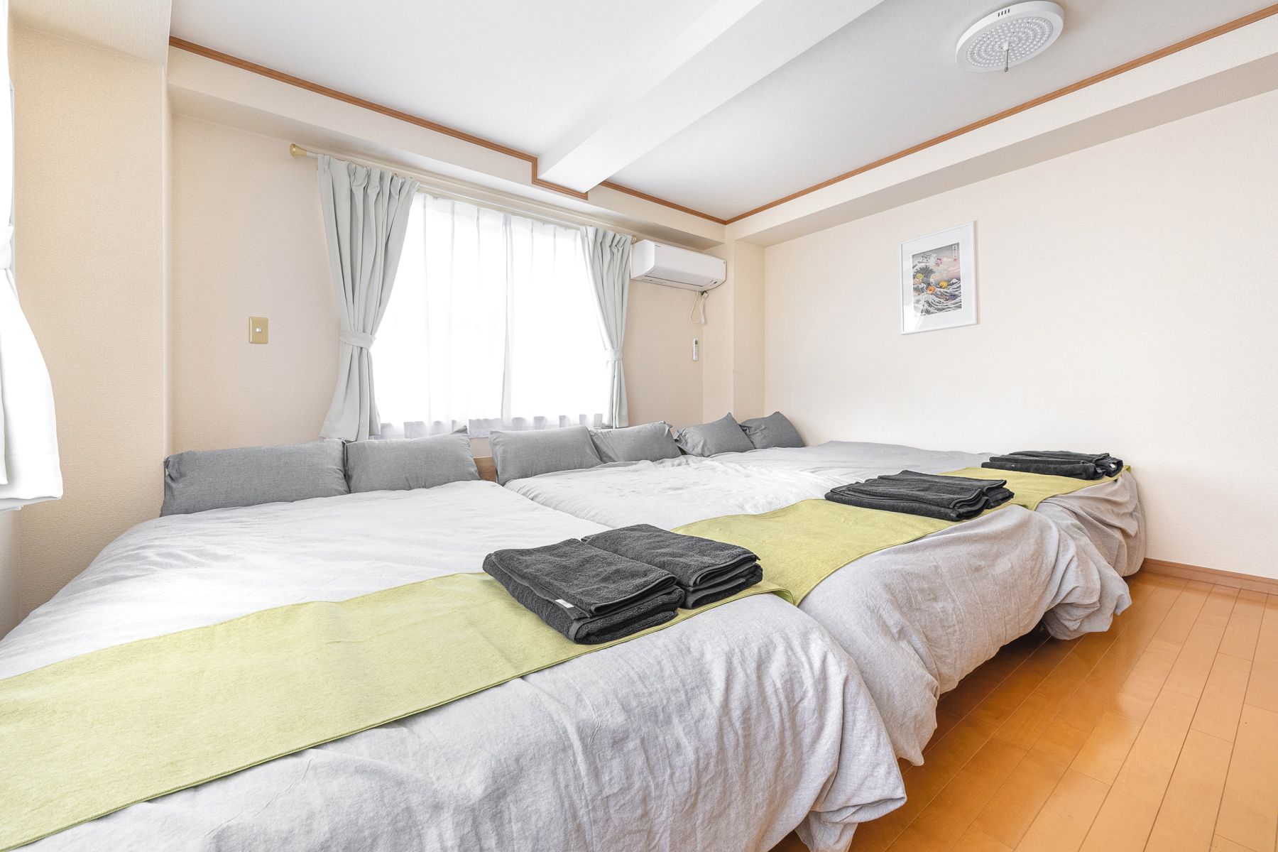 Quarto de hotel com uma cama grande, duas mesas de cabeceira, uma janela com cortinas, um aparelho de ar condicionado e um quadro na parede.