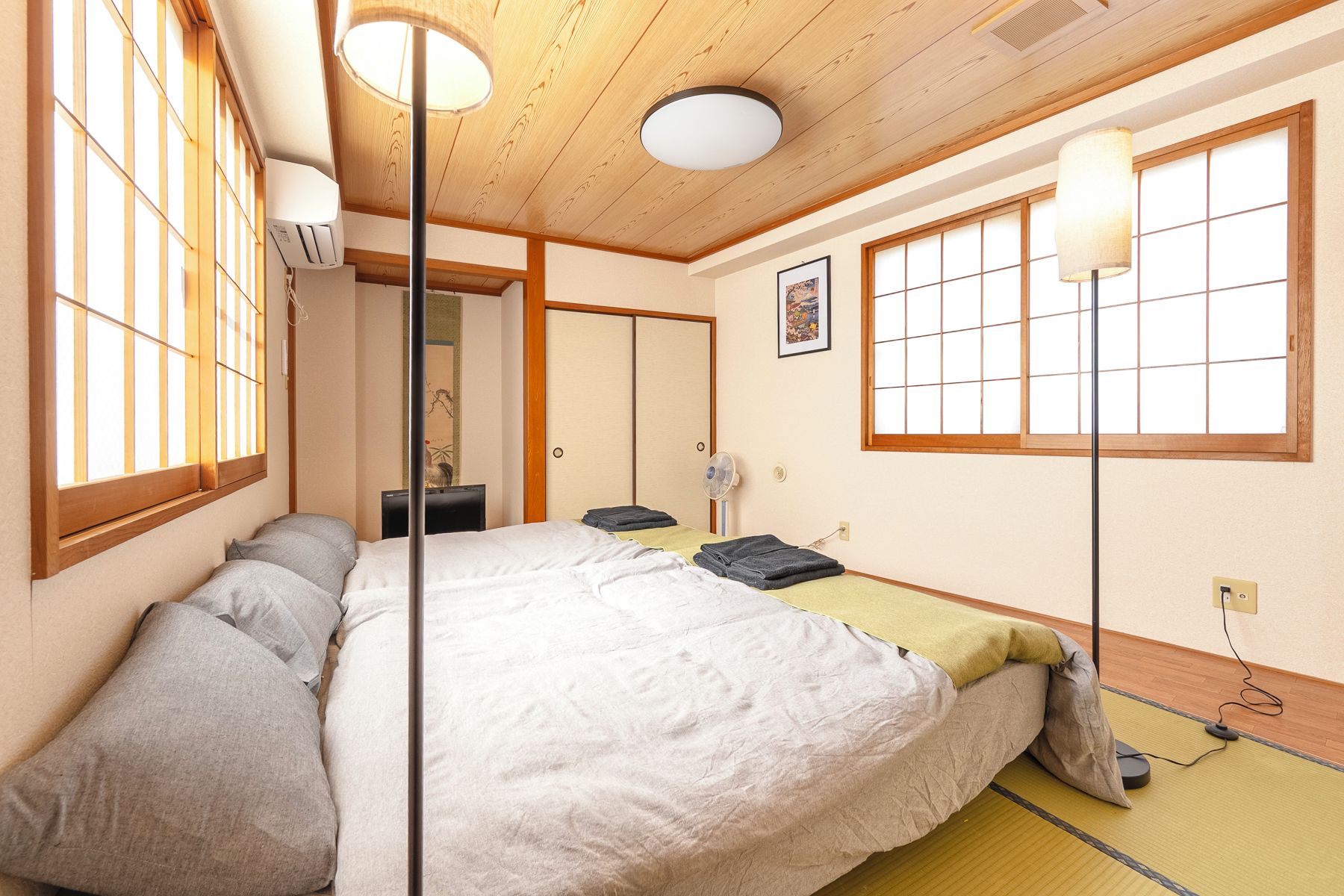 A traditional Japanese-style bedroom with tatami flooring, a futon bed, sliding doors, and a ceiling fan.