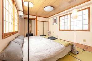 A traditional Japanese-style bedroom with tatami flooring, a futon bed, sliding doors, and a ceiling fan. - GrandHOUSE SHINJUKU 301 (Nakano City)