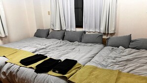 A bed with a grey duvet, a yellow blanket, and black bags on it. - GrandHOUSE SHINJUKU 301 (Nakano City)