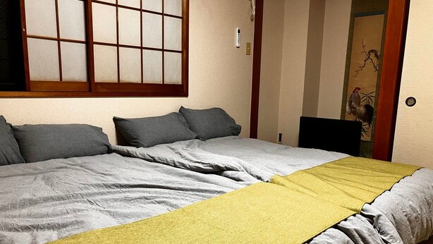 A room with two beds, a window with a grid pattern, and a door with a traditional design. - GrandHOUSE SHINJUKU 301 (Nakano City)