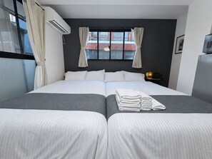 Une chambre d’hôtel comprenant un lit, deux tables de chevet, une fenêtre avec des rideaux, un appareil de climatisation et une lampe fixée au mur.