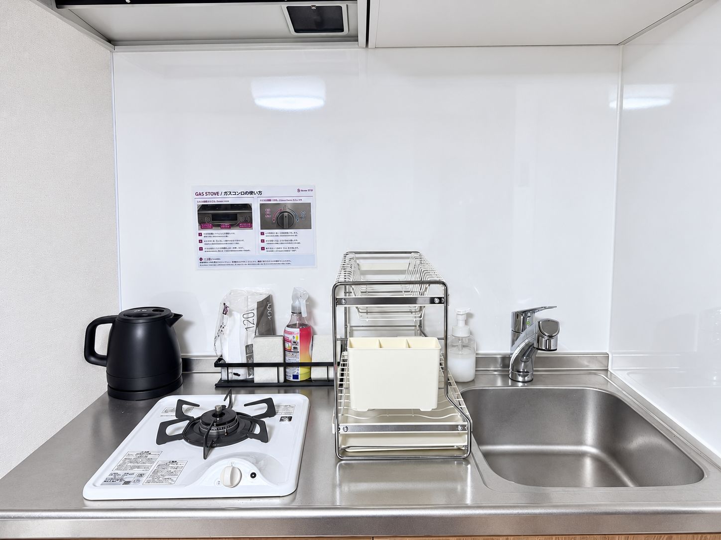 Uma cozinha compacta equipada com fogão a gás, chaleira, pia e escorredor de louça.