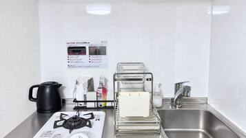 Uma cozinha compacta equipada com fogão a gás, chaleira, pia e escorredor de louça.