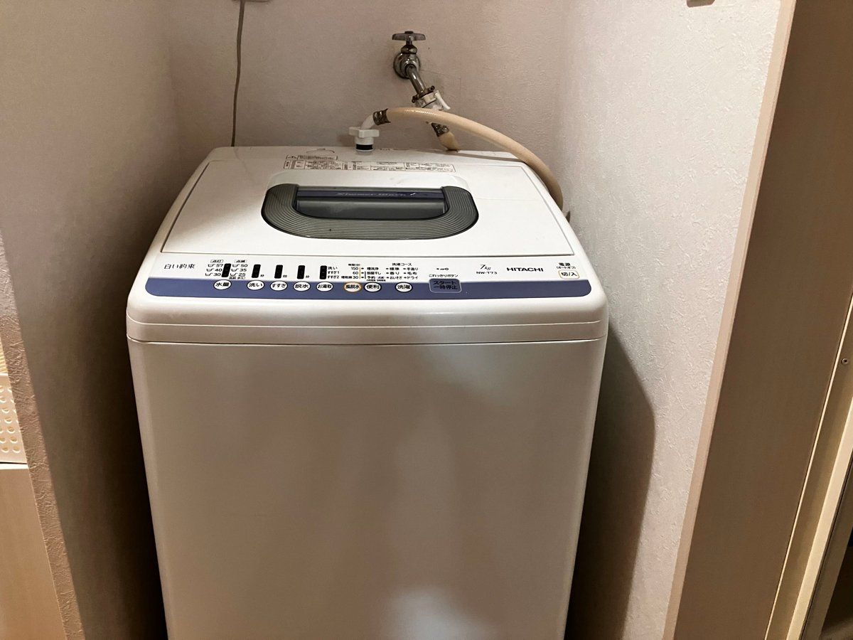 Máquina de lavar roupa compacta, branca e fixada na parede, com painel de controle e uma mangueira.