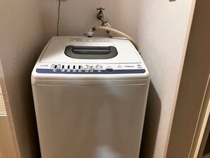 Une machine à laver blanche, compacte, conçue pour être fixée au mur, dotée d’un panneau de commande et d’un tuyau.