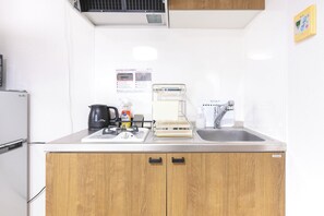 A kitchen with a gas stove, a coffee maker, a kettle, a sink, and a cabinet. - WabiSabiROOM SHINJUKU 201 (Nakano City)