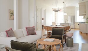 Una sala de estar moderna con un sofá, sillas, una mesa redonda y una cocina al fondo.