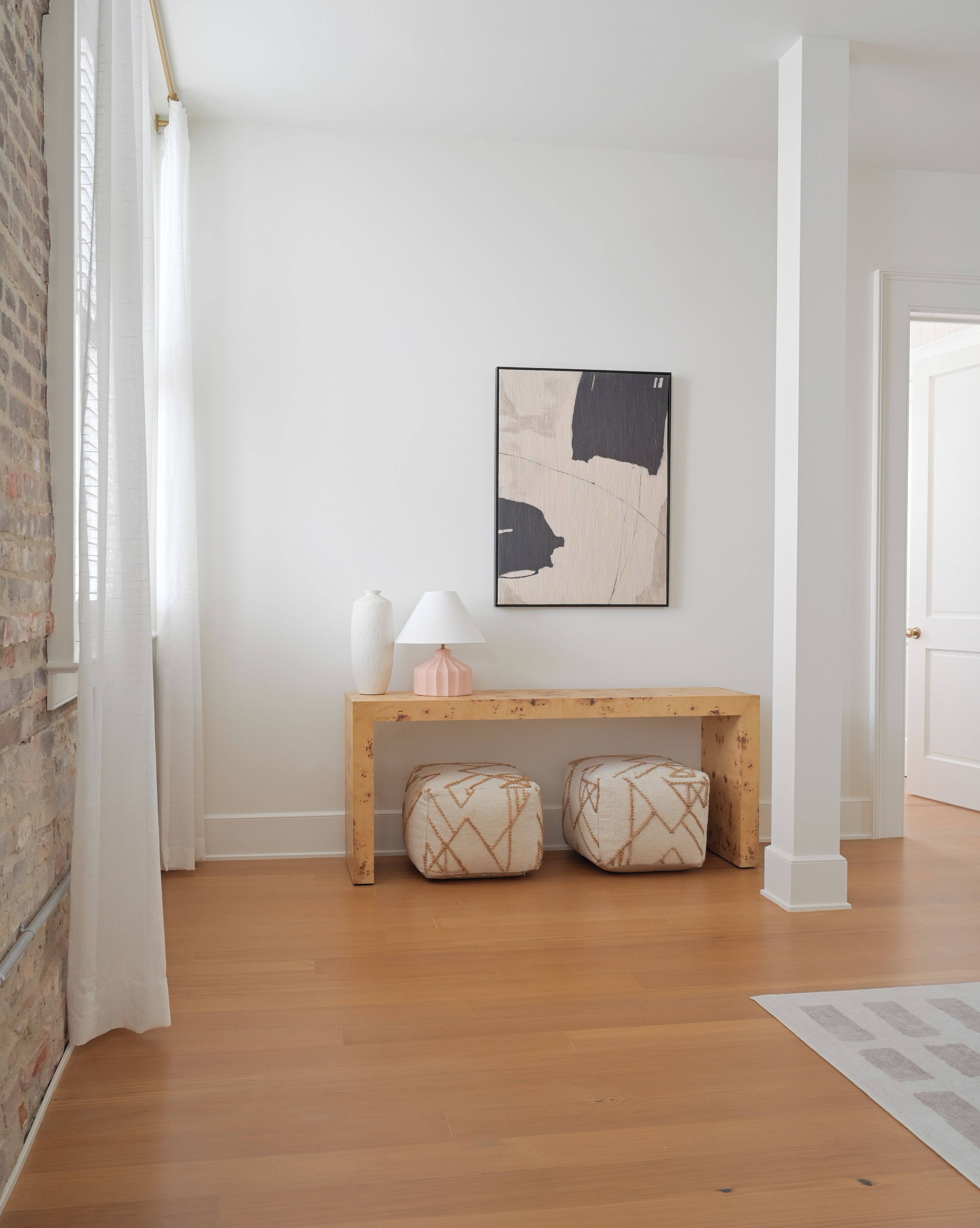 Una habitación con un banco de madera, dos cojines, un jarrón blanco y una lámpara.