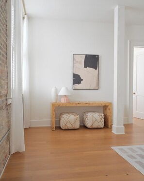 Una habitación con un banco de madera, dos cojines, un jarrón blanco y una lámpara.
