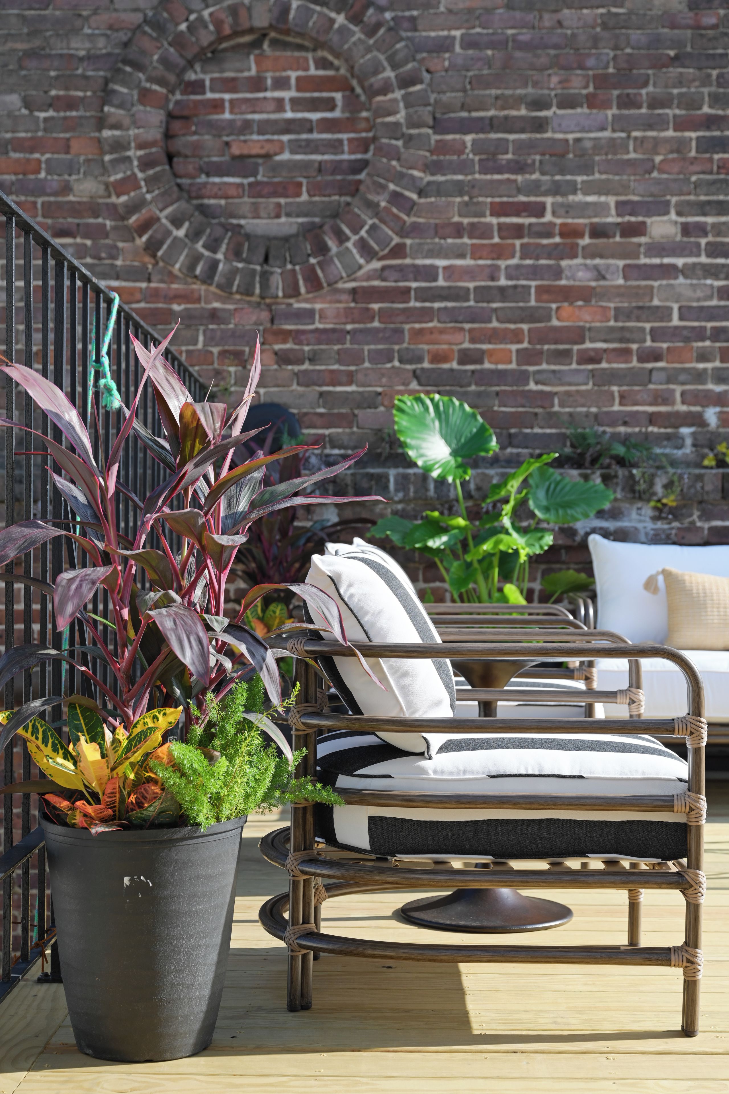 Un patio con una silla de mimbre, una planta en maceta y una pared de ladrillo con un ventanal circular.
