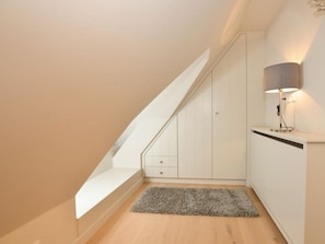A modern, minimalistic room with a sloped ceiling, a built-in bench, a small rug, and a wall-mounted lamp. - Witthus 15 - Stylish Living Under a Thatched Roof (Wenningstedt-Braderup)
