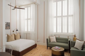 Un dormitorio moderno con una cama, un sofá verde, una mesita de centro redonda y un ventilador de techo.