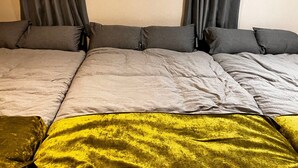 Uma cama com roupa de cama cinza e amarela, cortinas cinzas e uma parede lisa.