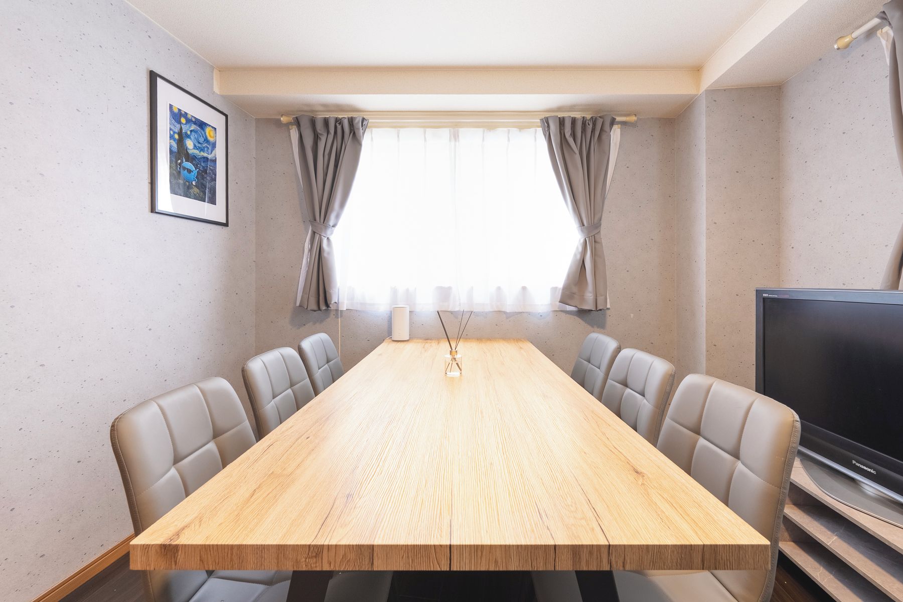 Uma sala de conferências com mesa de madeira, seis cadeiras, uma televisão e uma obra de arte emoldurada na parede.
