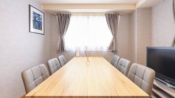 Uma sala de conferências com mesa de madeira, seis cadeiras, uma televisão e uma obra de arte emoldurada na parede.