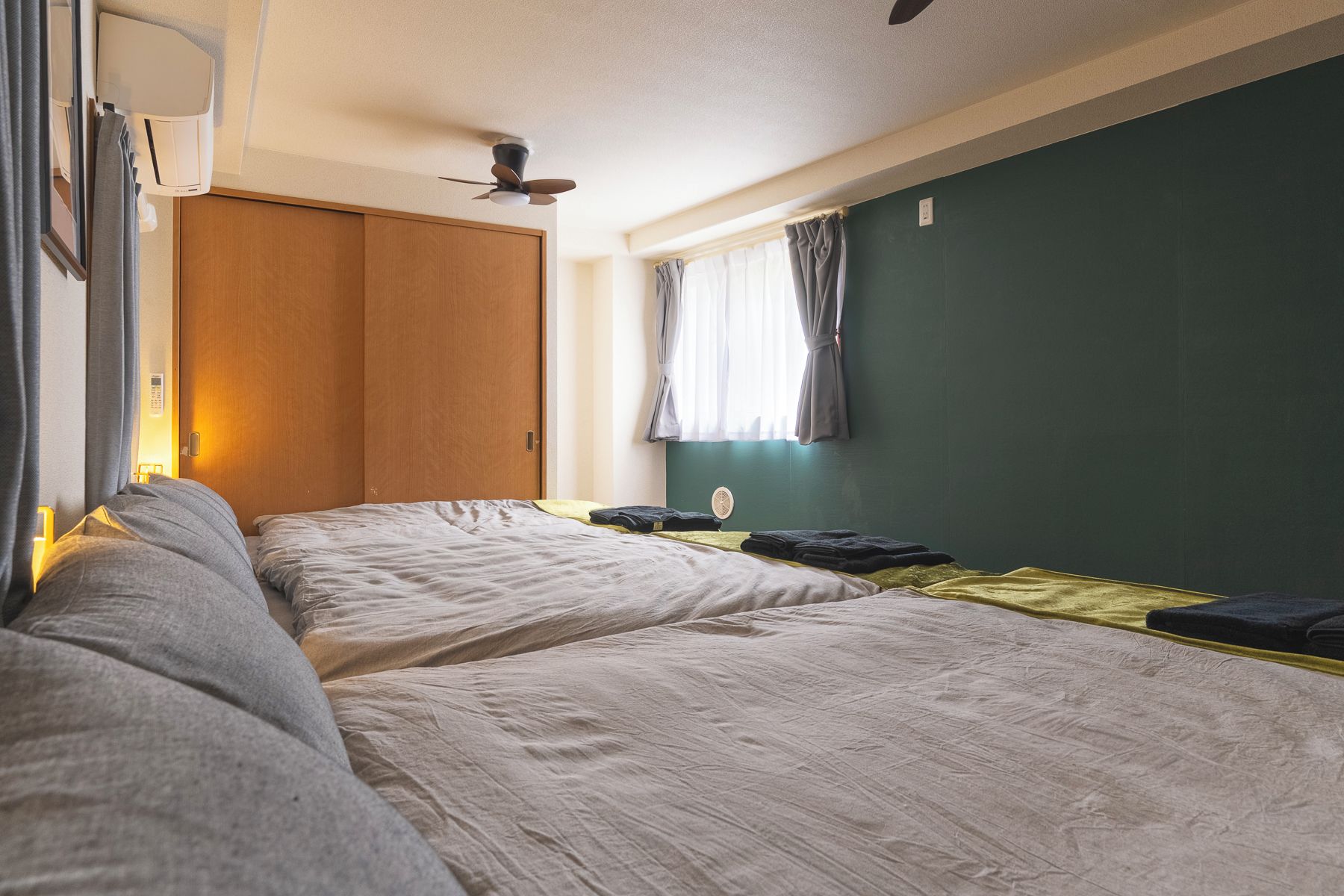 Quarto com duas camas, um guarda-roupa de madeira, um ventilador de teto e uma janela com cortinas.