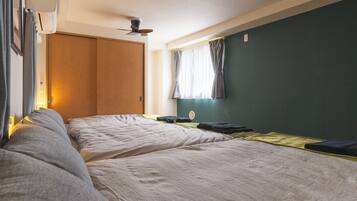 Quarto com duas camas, um guarda-roupa de madeira, um ventilador de teto e uma janela com cortinas.