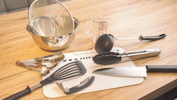 Uma mesa de madeira com utensílios de cozinha, incluindo um escorredor, medidor, espátula, pinças e uma faca.