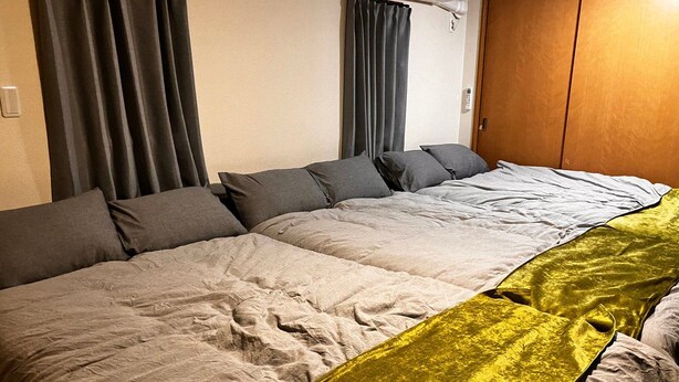 Uma cama grande com roupa de cama cinza e um cobertor amarelo de destaque.