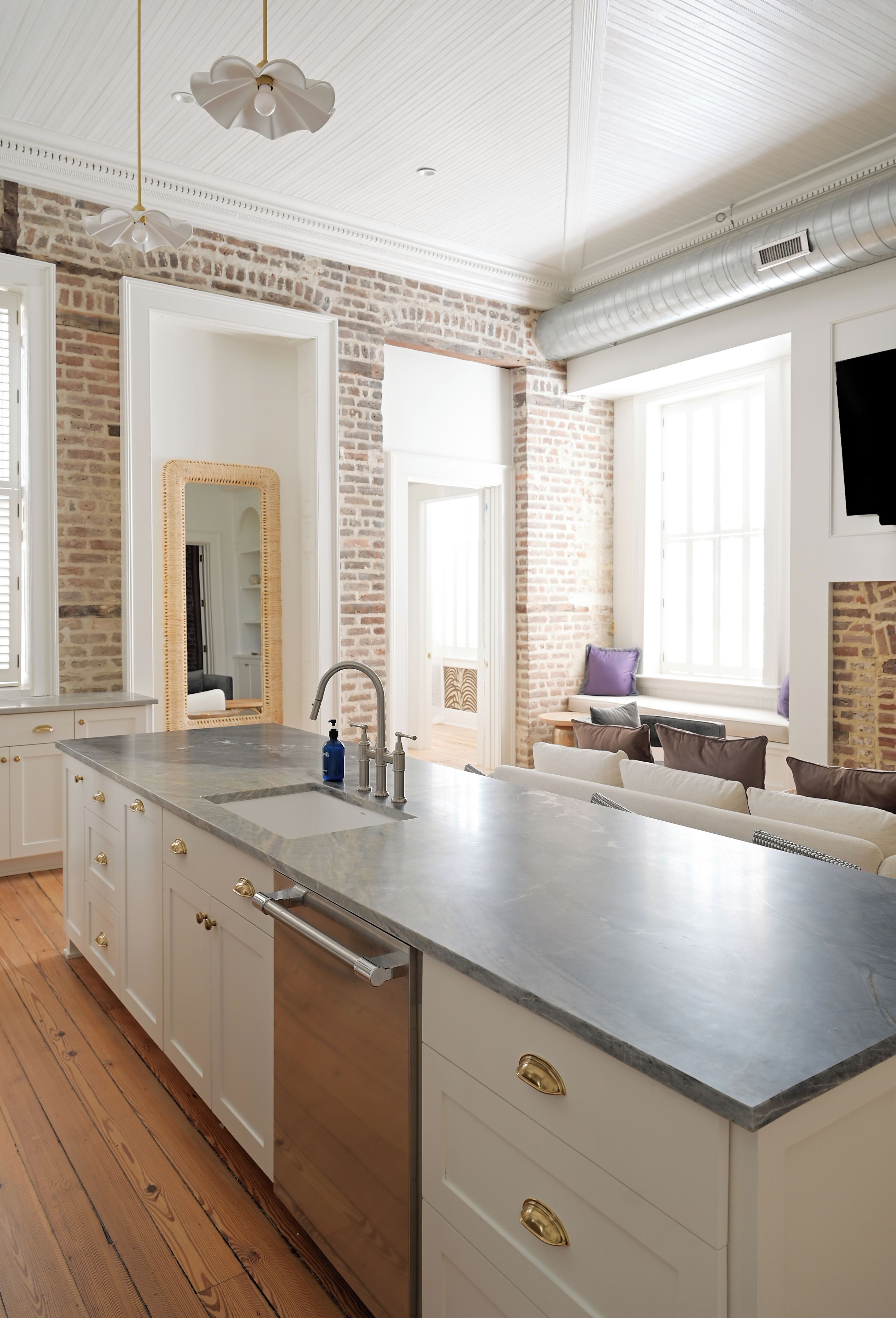 Una cocina moderna con una isla grande, muebles blancos y una pared de ladrillo decorativa.