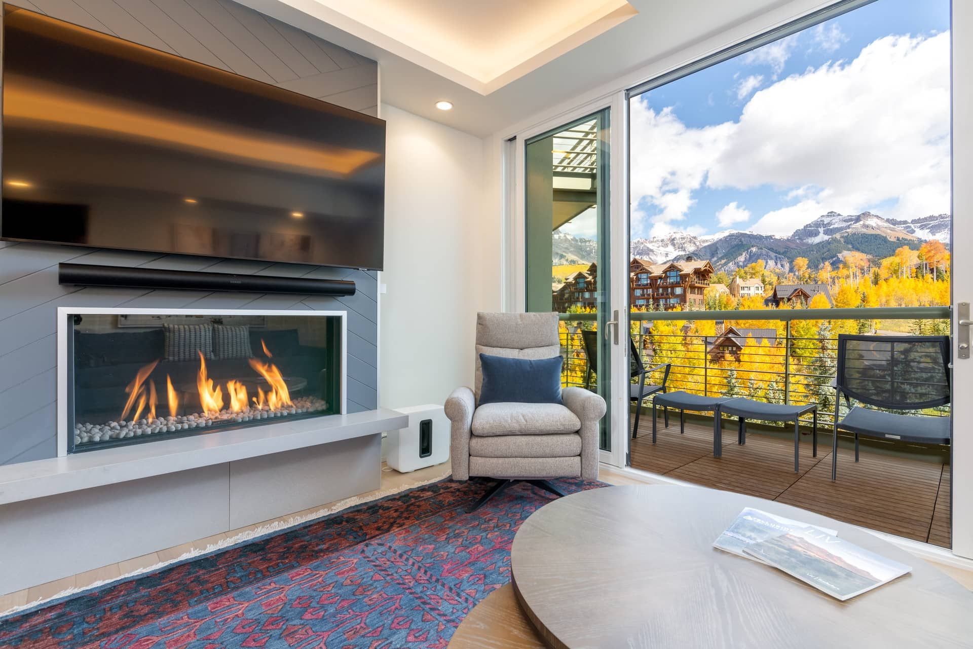 Un interior moderno con chimenea, un sillón cómodo y un balcón con vistas panorámicas a la montaña.