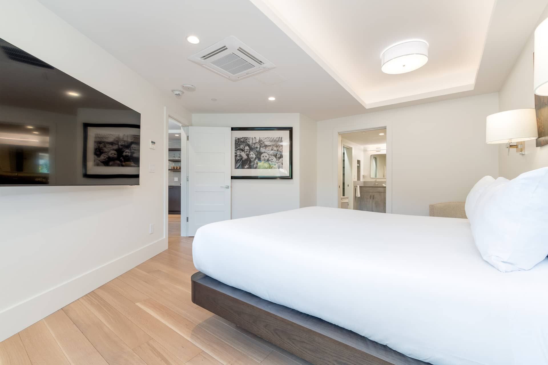 A modern hotel room with a large bed, a bathroom with a mirror, and a hallway leading to another room.