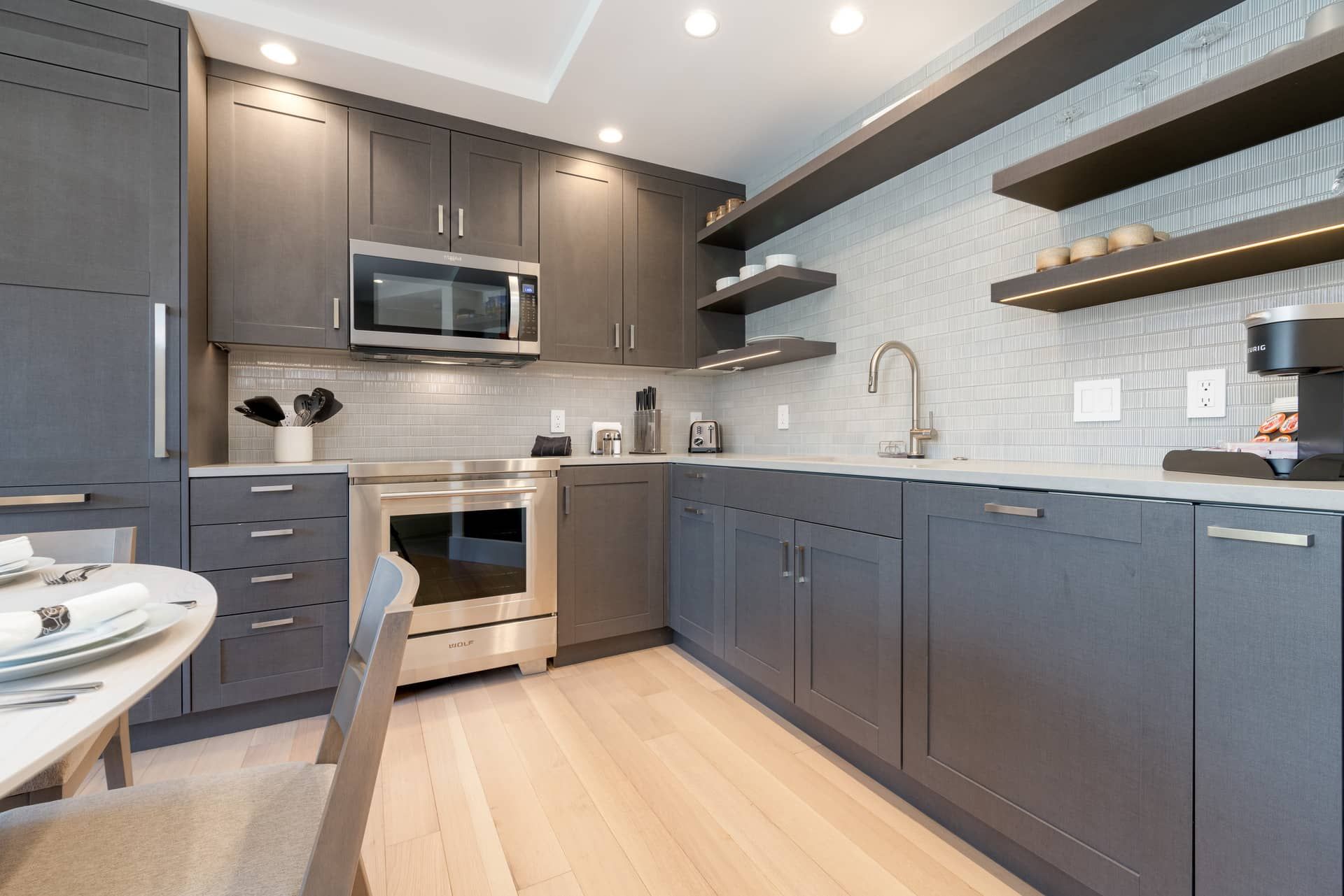 A modern kitchen with grey cabinetry, stainless steel appliances, and a tiled backsplash.