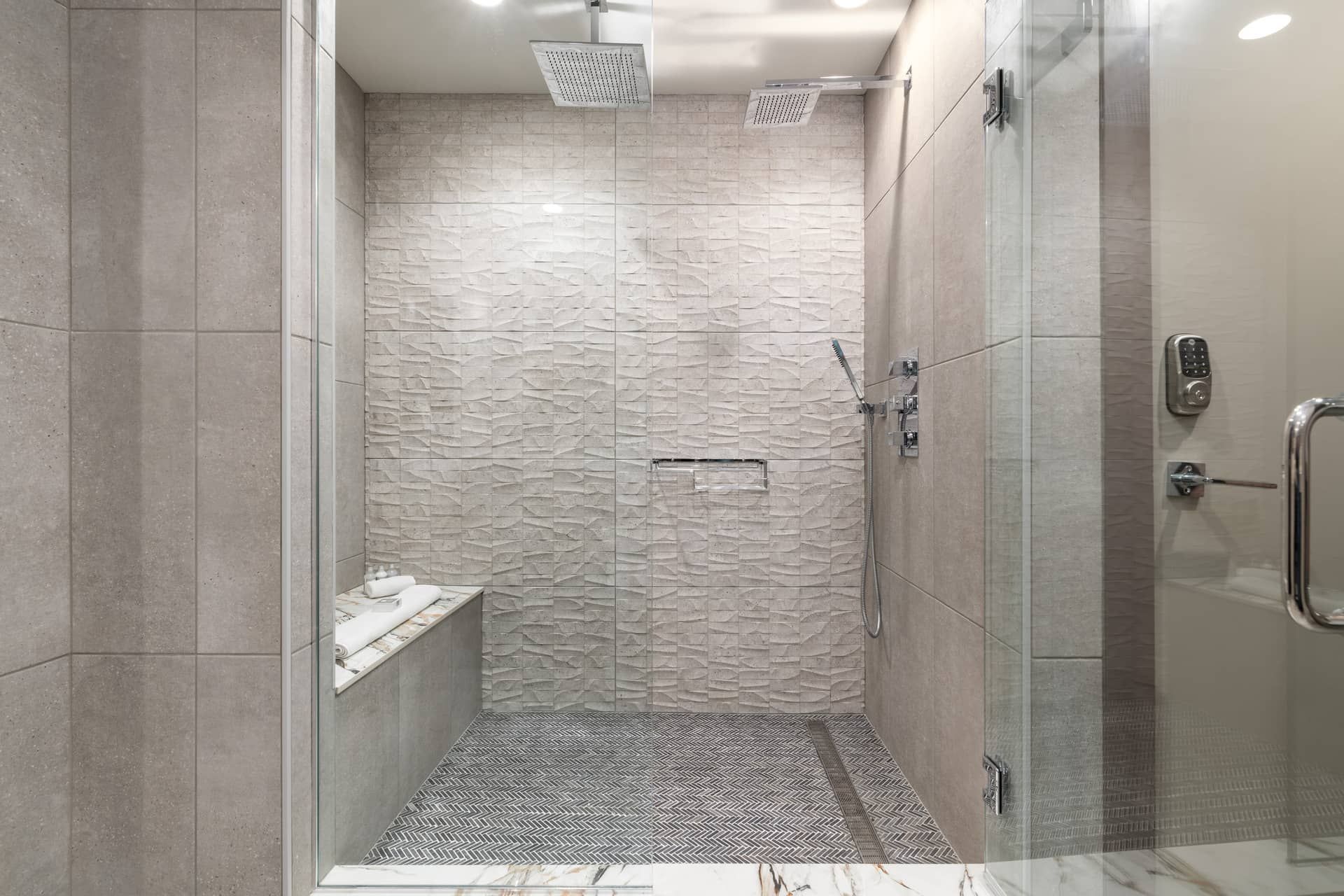 Une douche moderne avec un mur texturé, une porte en verre et un sol à motifs en chevrons.