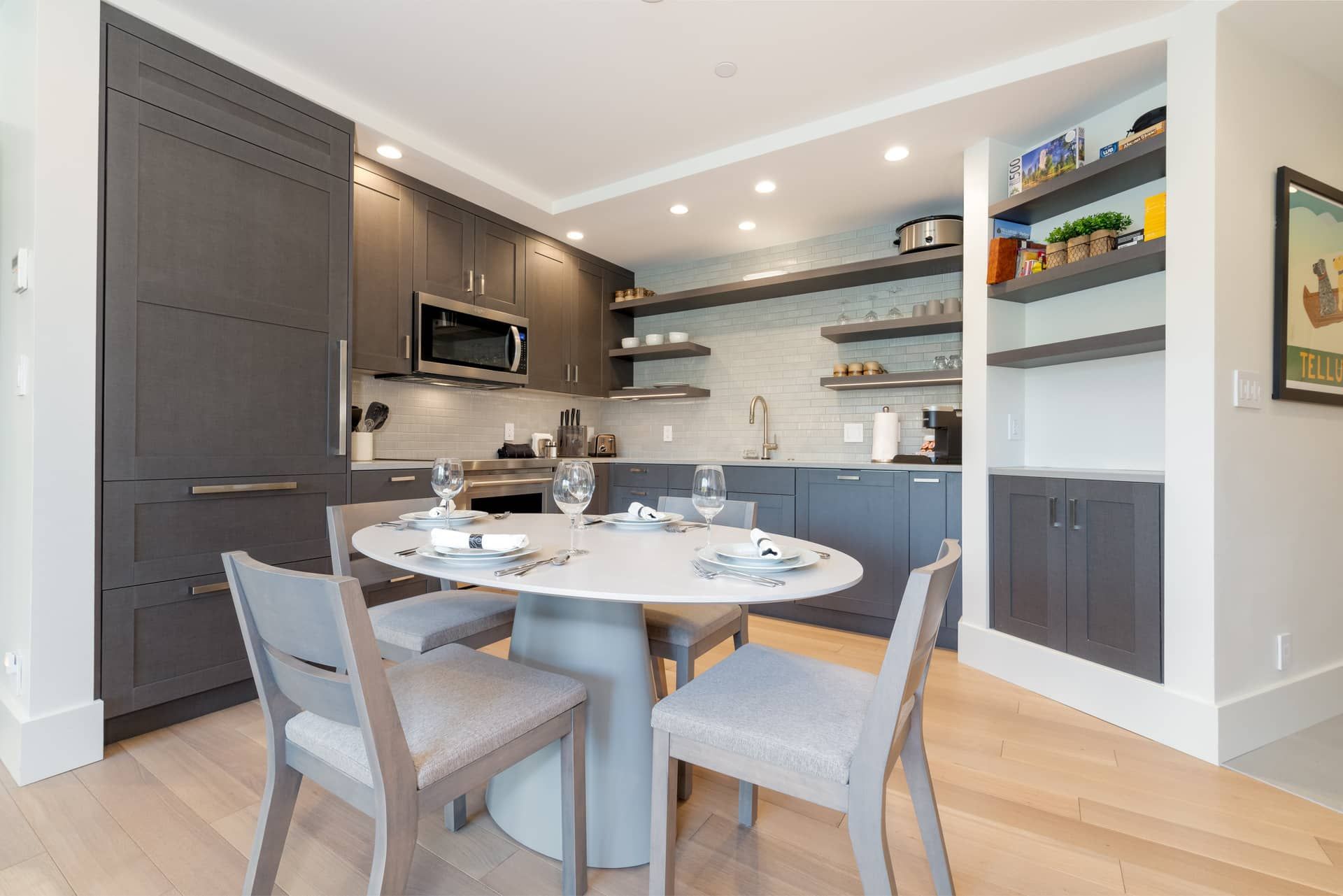 Una cocina moderna con armarios oscuros, una isla central y un comedor con cuatro sillas.