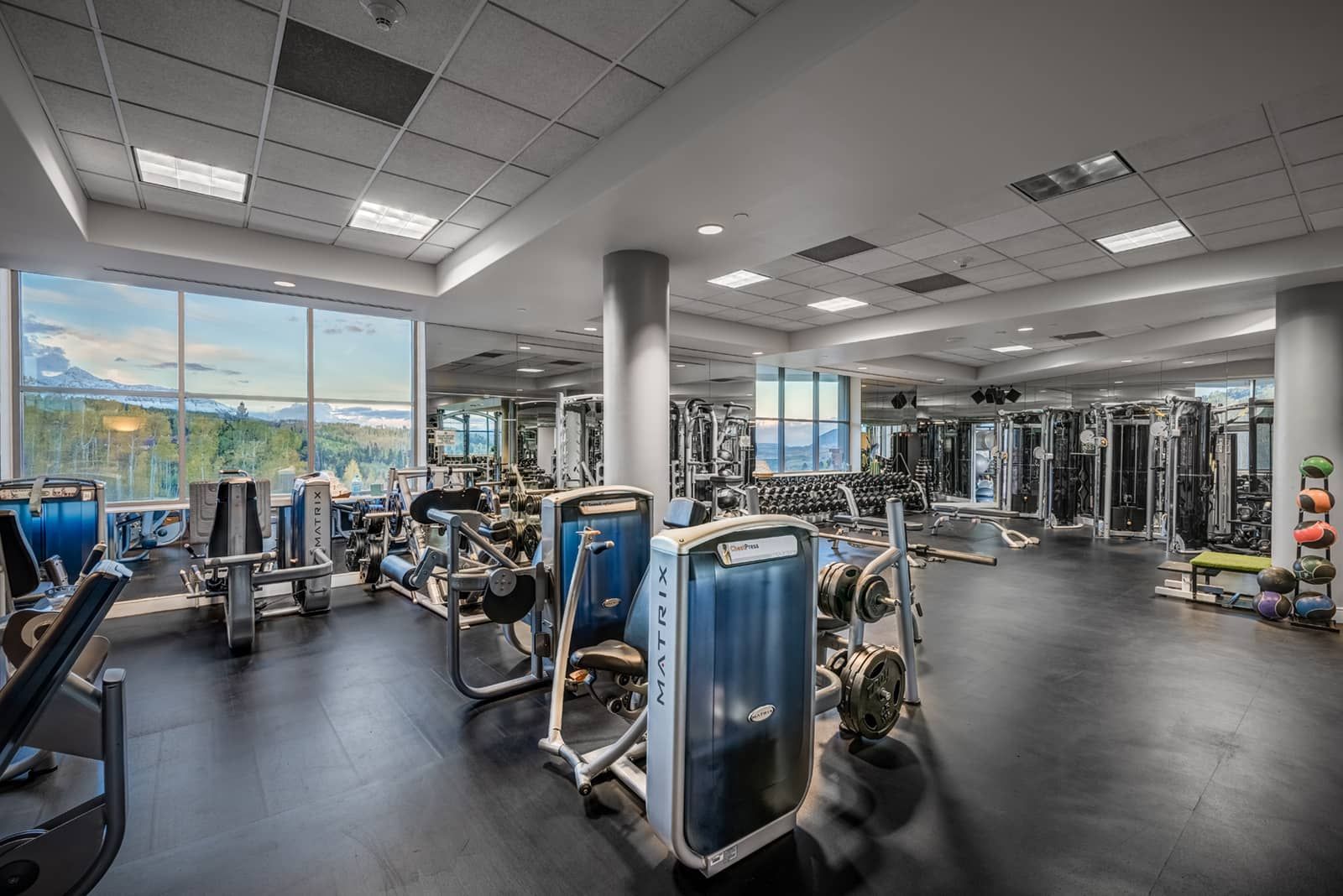 A gym with various exercise equipment, large windows, and a view of the outdoors.