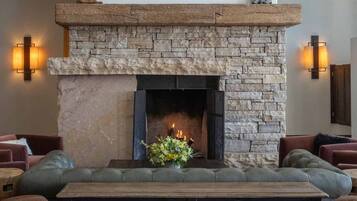 A stone fireplace with a mantel, surrounded by leather sofas and a wooden stool.
