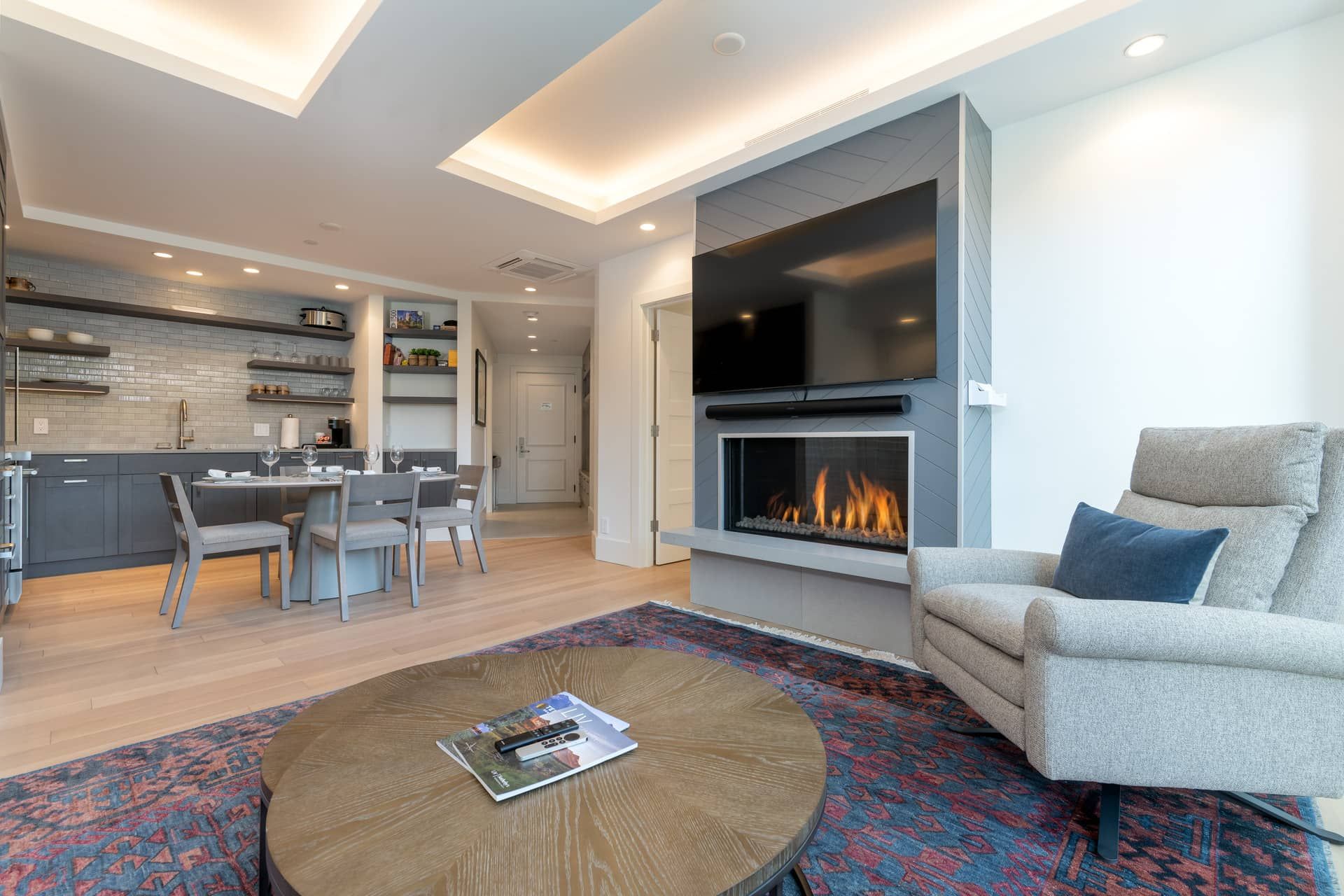 A modern living room with a fireplace, a dining area, and a kitchen.