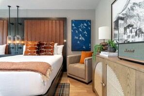 A modern hotel room with a bed, a seating area, a desk with a lamp, and artwork on the walls.