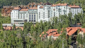 Ett hotell med flera våningar och en central innergård, omgivet av träd och med en imponerande bergskedja som bakgrund.