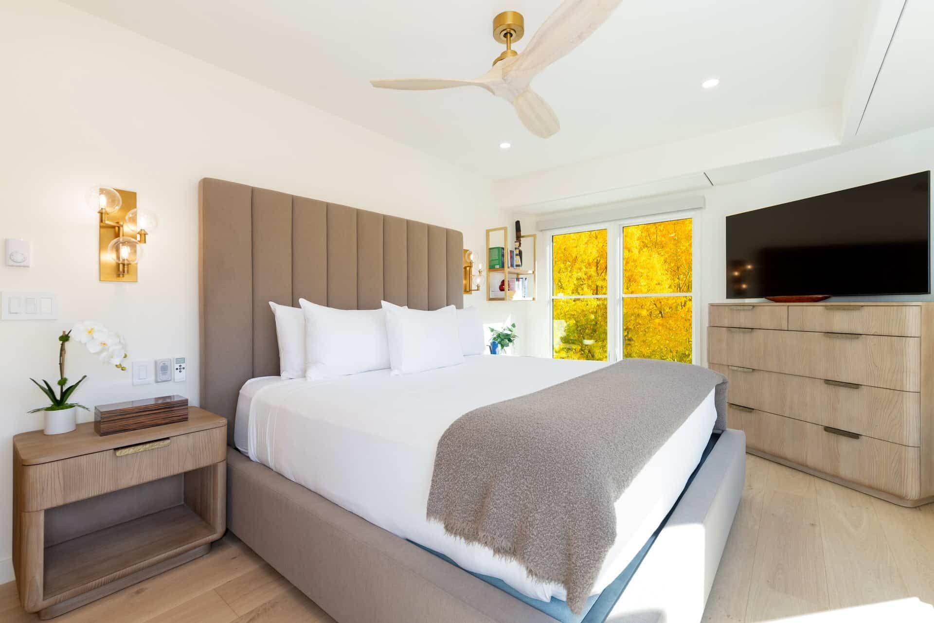 A modern bedroom with a bed, bedside table, nightstand, TV, and a ceiling fan.