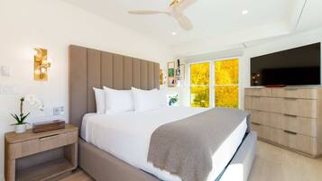 A modern bedroom with a bed, bedside table, nightstand, TV, and a ceiling fan.