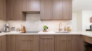 A modern kitchen with wooden cabinets, a built-in oven, a coffee maker, and a sink with gold fixtures.
