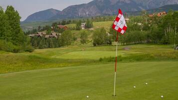 A golf course with a flagstick, a flag, and a distant mountain range.